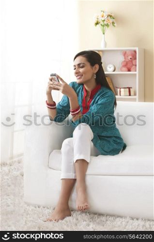 Full length of happy young woman using mobile phone on sofa