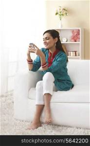 Full length of happy young woman using mobile phone on sofa