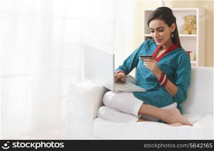 Full length of Indian woman with credit card shopping online in living room