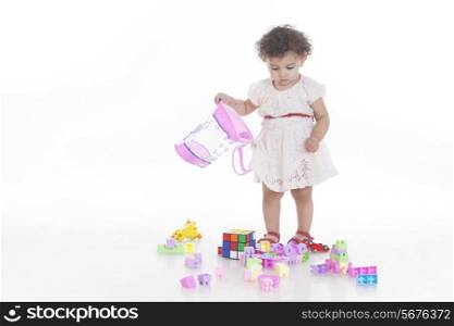 Full length of innocent cute girl looking at toys on floor against white background