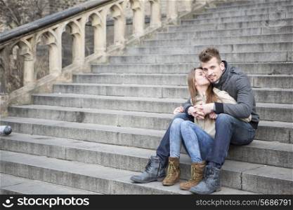 Full length of loving woman kissing man while sitting on steps outdoors