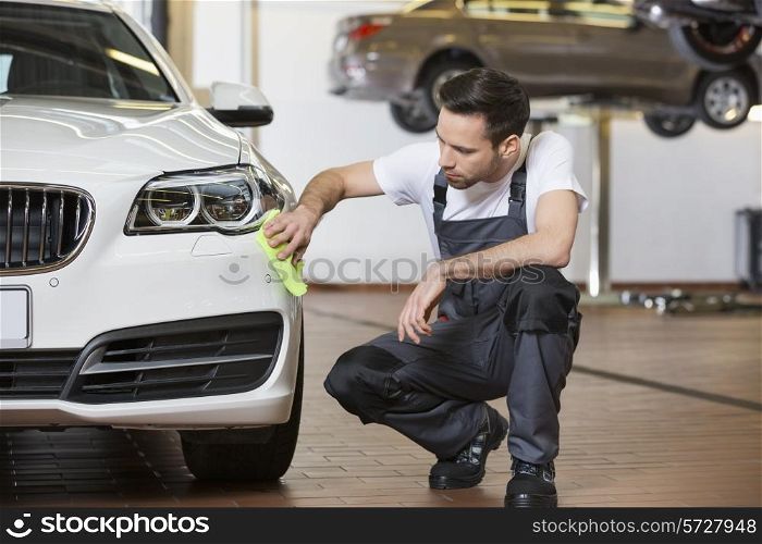 Full length of maintenance engineer cleaning car in workshop