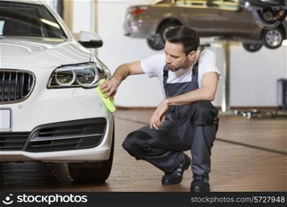 Full length of maintenance engineer cleaning car in workshop