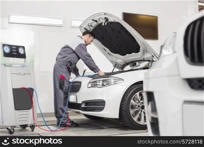 Full length of male engineer examining car in automobile repair shop