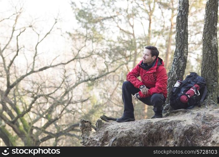 Full length of male hiker crouching on cliff in forest