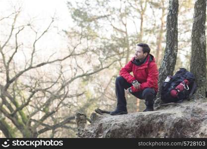 Full length of male hiker crouching on cliff in forest