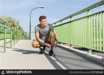 Full length of male jogger tying shoelace on bridge