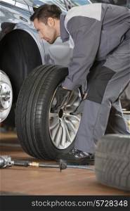 Full length of male mechanic fixing car&rsquo;s tire in repair shop