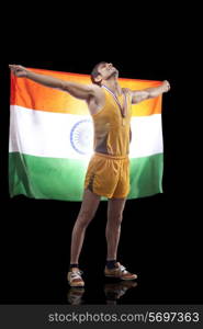 Full length of male medalist holding Indian flag as he looks up over black background