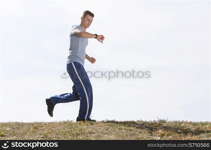 Full length of man checking time while jogging against sky