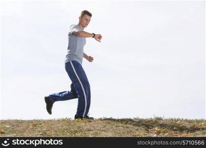 Full length of man checking time while jogging against sky