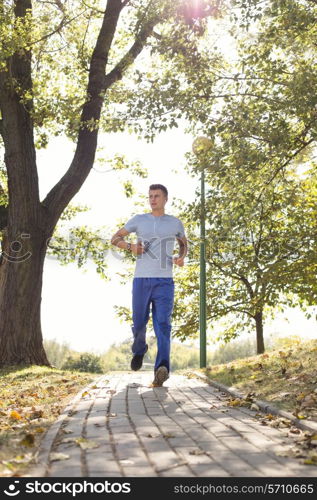 Full length of man listening music while jogging on path in park