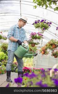 Full-length of man watering flower plants in greenhouse