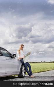 Full length of mid adult woman leaning on car while reading map at countryside