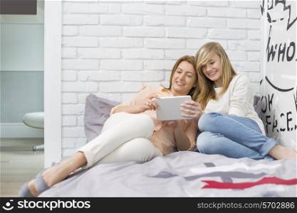 Full-length of mother with daughter using tablet PC in bedroom