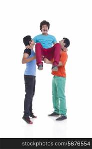 Full length of playful young men lifting male friend over white background