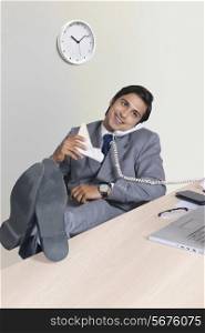 Full length of relaxed businessman answering telephone at office desk