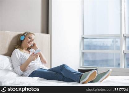 Full length of relaxed woman listening music in bedroom