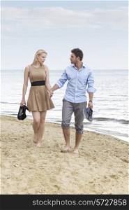 Full length of romantic young couple holding hands and walking on beach