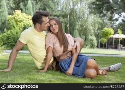 Full length of romantic young couple relaxing on grass in park