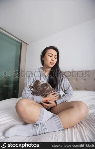 Full length of sad young woman with hot water bottle on stomach in bedroom