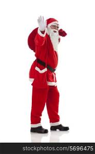 Full length of Santa Claus waving while carrying sack full of presents over white background