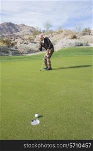 Full length of senior male golfer celebrating sinking putt at golf course
