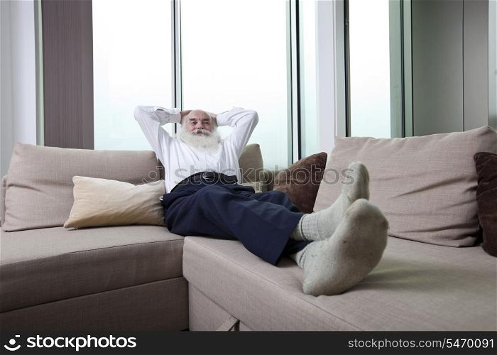 Full length of senior man reclining on sofa with hands behind head at home