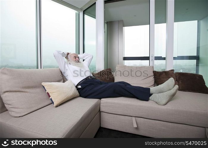 Full length of senior man relaxing on sofa with hands behind head at home