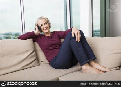 Full-length of senior woman answering smart phone on sofa at home