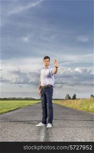 Full length of serious young man holding up hand to stop at country road