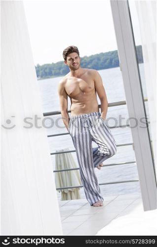 Full length of shirtless young man leaning on railing of hotel balcony