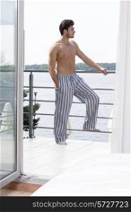 Full length of shirtless young man on hotel balcony looking away