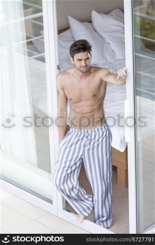 Full length of shirtless young man standing at balcony doorway