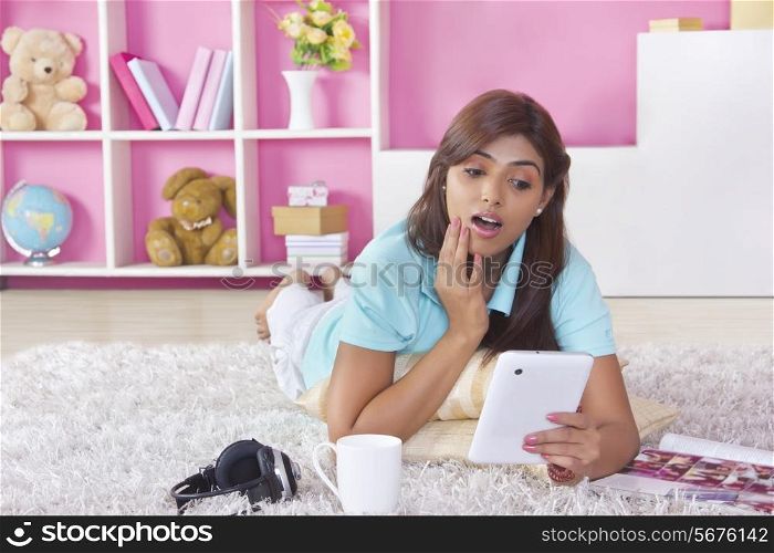 Full length of shocked woman using digital tablet at home
