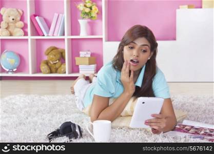 Full length of shocked woman using digital tablet at home