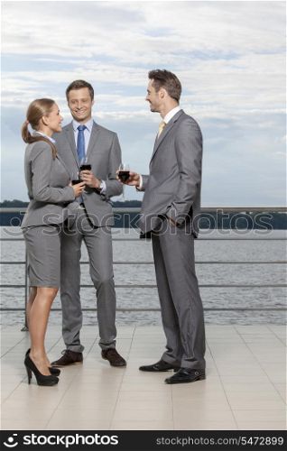 Full length of smiling businesspeople with wineglasses standing on terrace