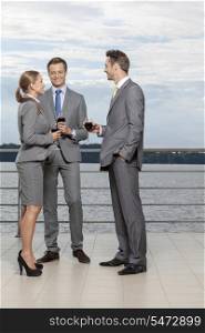 Full length of smiling businesspeople with wineglasses standing on terrace