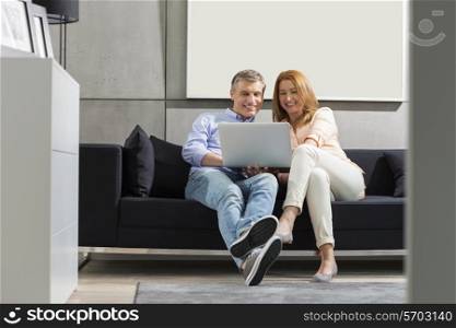 Full-length of smiling couple using laptop on sofa