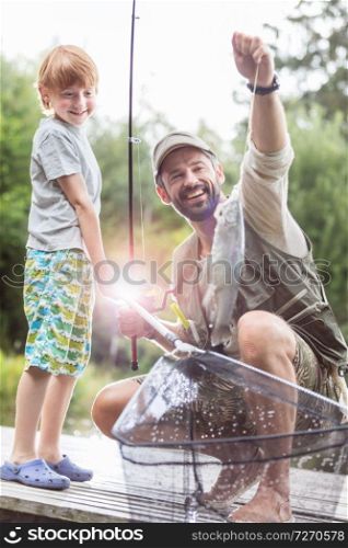 Full length of smiling father and son fishing on pier