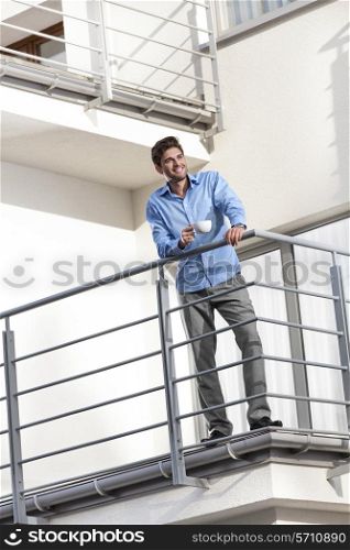 Full length of smiling young businessman having coffee at hotel balcony