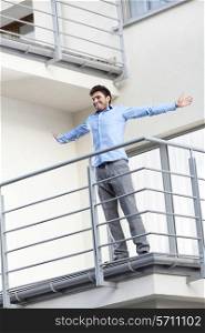 Full length of smiling young businessman standing arms outstretched at hotel balcony
