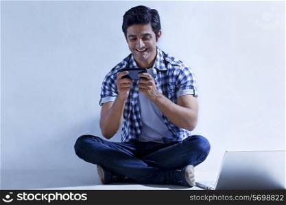 Full length of smiling young man sitting by laptop reading text message