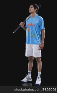 Full length of sportsman looking away while holding hockey stick over black background