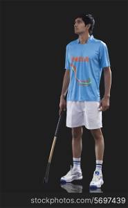 Full length of sportsman with hockey stick looking away over black background