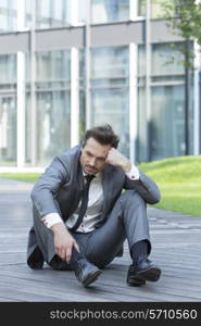 Full length of stressed businessman sitting on path outside office