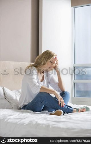 Full length of stressed woman with hand on face sitting on bed