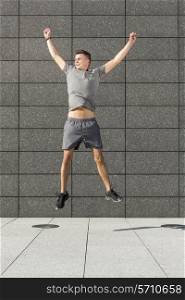 Full length of successful jogger jumping against tiled wall