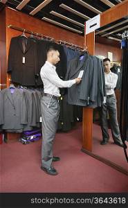 Full-length of tailor standing by the clothing rack of suits