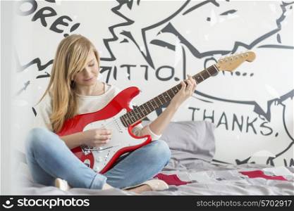 Full-length of teenage girl playing guitar in bedroom